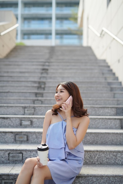 Belle femme parlant sur smartphone et tenant une tasse de papier