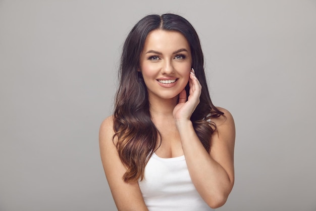 Belle femme avec une peau propre, des cheveux longs et un sourire sharming se dresse sur un fond gris isolé