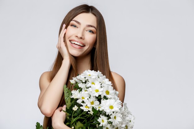 Belle femme avec une peau propre et fraîche tenant des fleurs