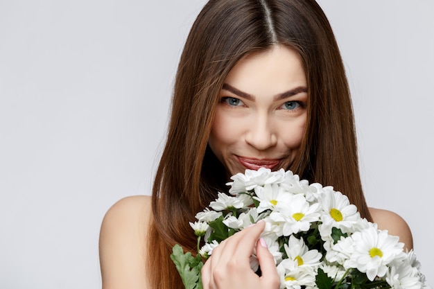 Belle femme avec une peau propre et fraîche tenant des fleurs