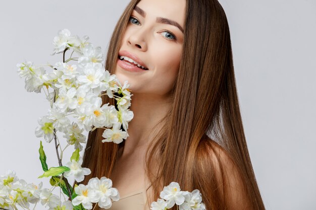 Belle femme avec une peau propre et fraîche tenant des fleurs