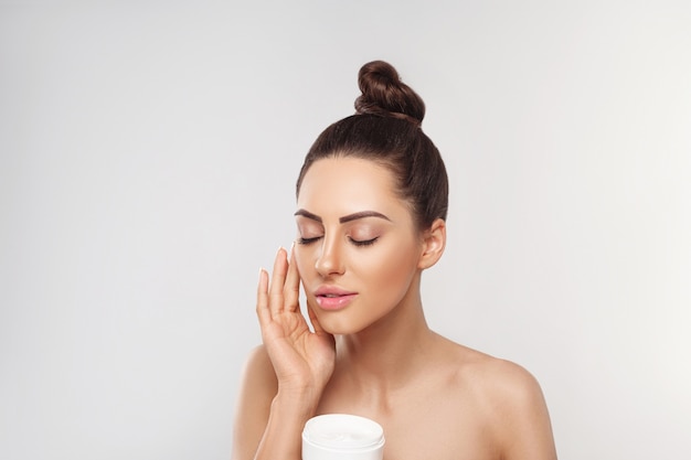 Belle femme avec une peau saine du visage lisse et propre tenant une bouteille de crème cosmétique