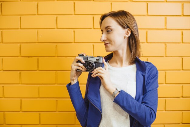 Belle femme avec photocamera film rétro sur mur de briques jaunes