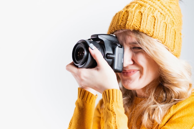 Une belle femme photographe dans un chapeau tricoté est photographiée avec un appareil photo dans les mains dans un studio photo