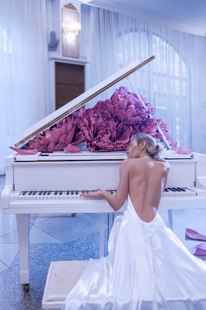 Belle femme avec piano blanc et fleurs de pivoines en studio blanc