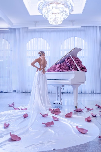 Belle femme avec piano blanc et fleurs de pivoines en studio blanc