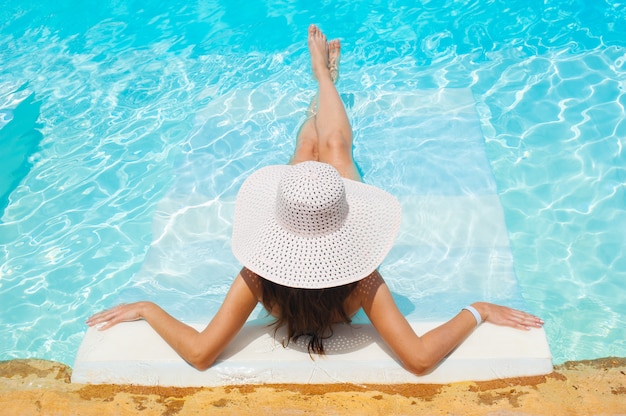 Belle femme portant un chapeau blanc et un bikini allongé dans une piscine