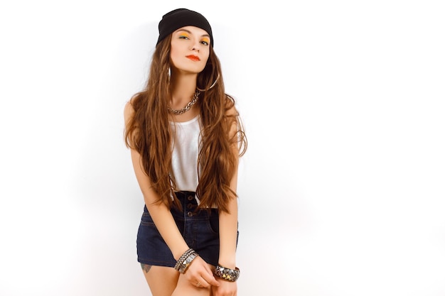 Belle femme portant un chapeau noir et un t-shirt blanc debout près du mur blanc