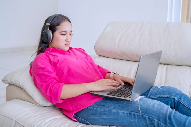 Une belle femme portant des écouteurs tapant sur un ordinateur portable à la maison