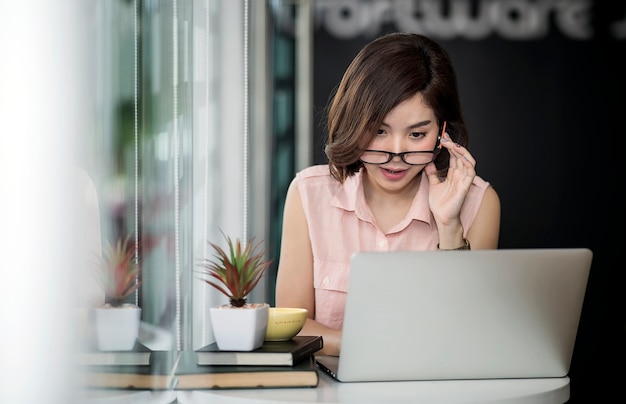 Belle femme portant des lunettes en regardant l&#39;écran tout en travaillant avec un ordinateur portable