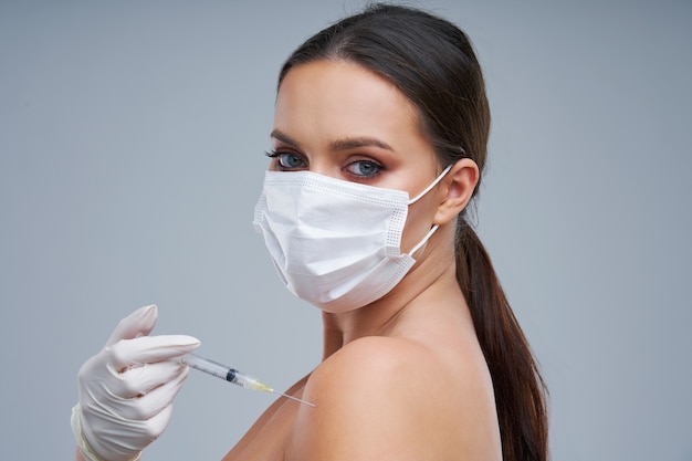 belle femme portant un masque et tenant un vaccin sur fond gris