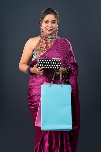 Belle femme portant un sari tenant des sacs à provisions et une boîte-cadeau sur fond gris