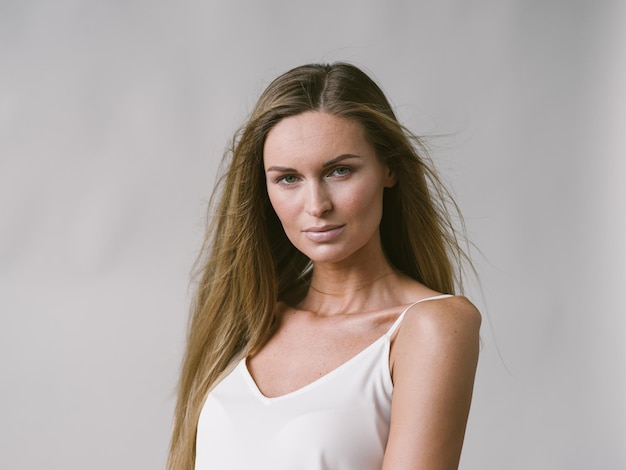 Belle femme portrait naturel fille aux longs cheveux blonds sur mur gris blanc. Prise de vue en studio.