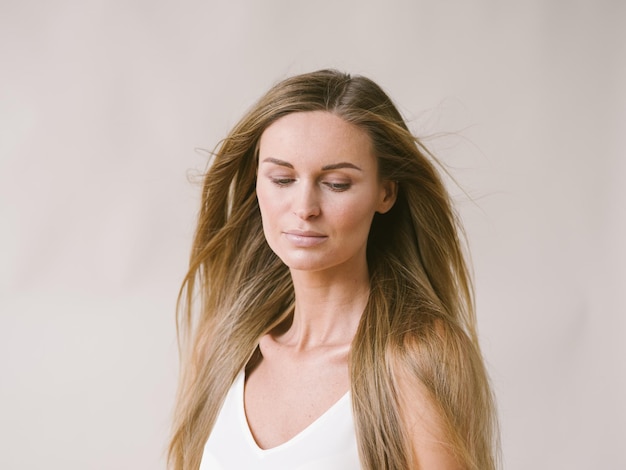 Belle femme portrait naturel fille aux longs cheveux blonds sur mur gris blanc. Prise de vue en studio.