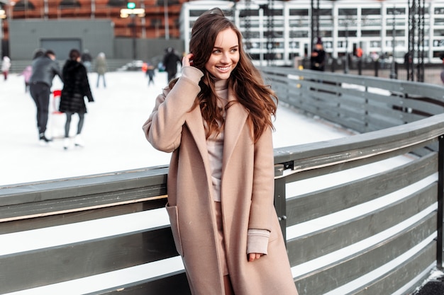 Photo belle femme posant seul et souriant en hiver dans le parc près de la patinoire