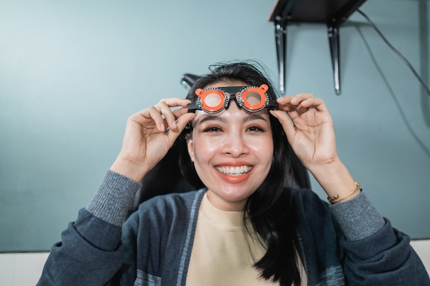 Une belle femme pose tenant des verres à mesurer qui sont utilisés dans une pièce d'une clinique ophtalmologique