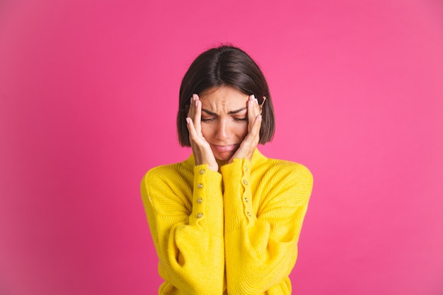 Belle femme en pull jaune vif isolée sur une dépression de pleurs stressante rose