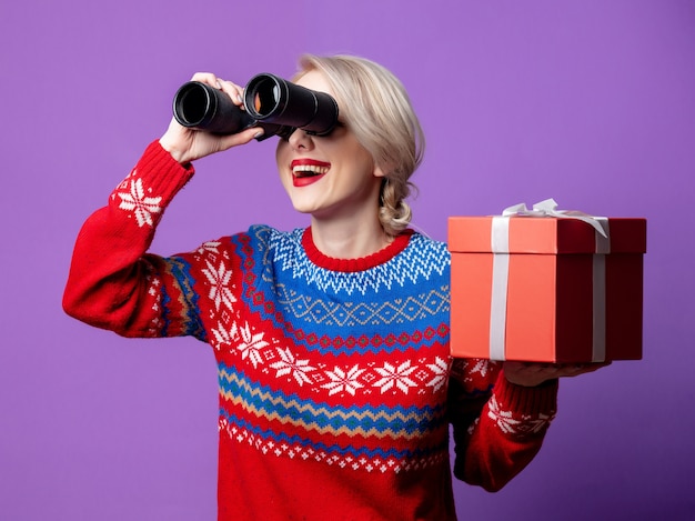 Belle femme en pull de Noël avec boîte-cadeau et jumelles