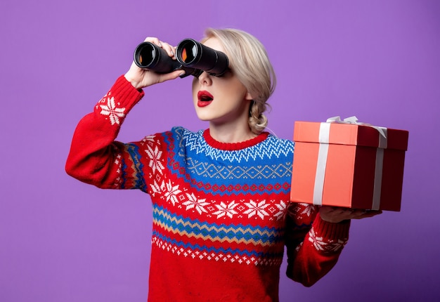 Belle femme en pull de Noël avec boîte-cadeau et jumelles