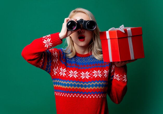 Belle femme en pull de Noël détient une boîte-cadeau et des jumelles