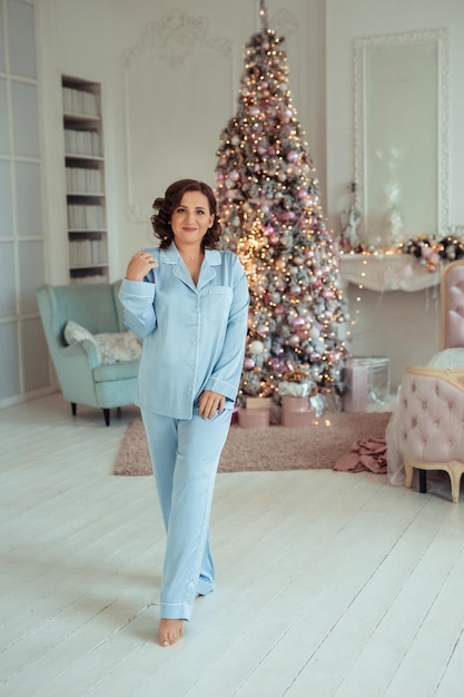 Belle femme en pyjama de soie bleu dans une chambre décorée près du sapin de Noël