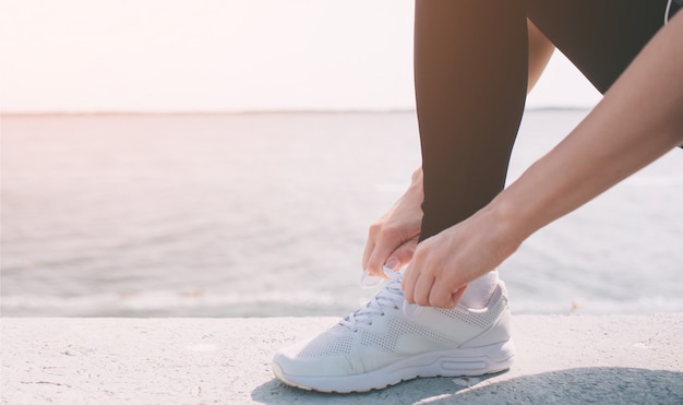 Belle femme qui court pendant le coucher du soleil. Jeune modèle de fitness près de bord de mer. Vêtu de vêtements de sport. Baskets cordes