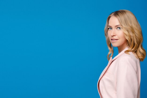 Belle femme de race blanche aux cheveux ondulés clairs dans une chemise blanche isolée sur fond bleu