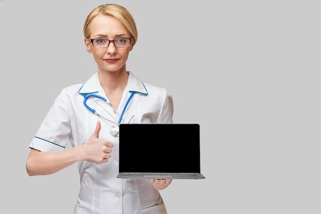 Belle femme de race blanche médecin ou infirmière tenant un ordinateur portable avec écran blanc