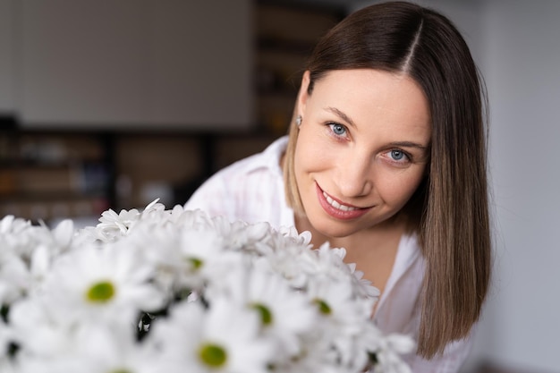 Belle femme de race blanche sent les fleurs qu'elle est heureuse d'obtenir un bouquet frais de chrysanthème blanc