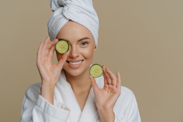 Une belle femme rafraîchie positive détient des tranches de concombre frais fait un masque pour la peau du visage