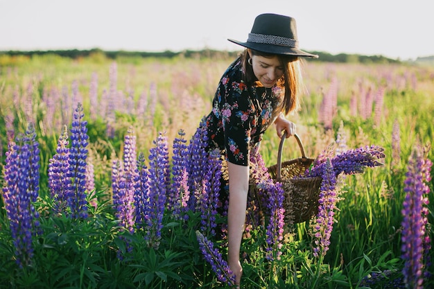 Photo belle femme rassemblant du lupin dans un panier rustique dans un champ ensoleillé se relaxant dans la campagne estivale