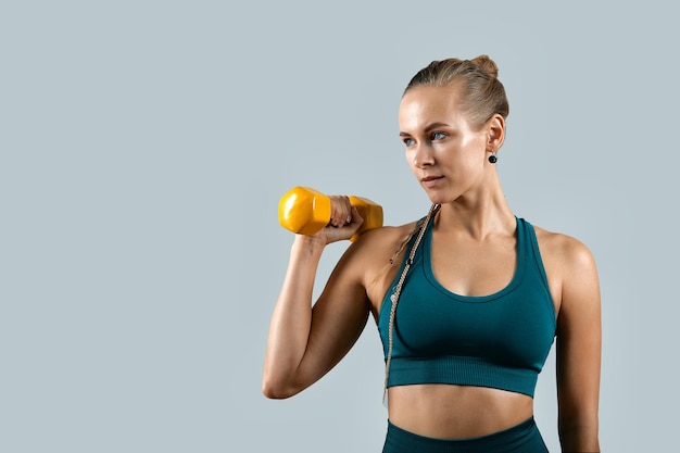 Belle femme de remise en forme athlétique avec des haltères dans ses mains posant devant la caméra sur fond gris