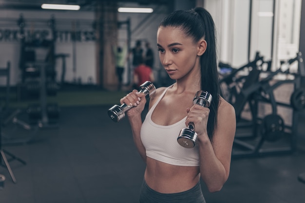 Belle femme de remise en forme à la recherche concentrée, entraînement avec haltères, espace copie