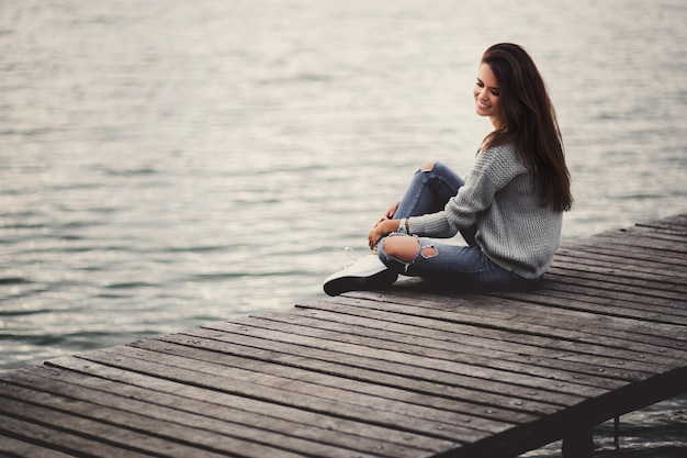 Belle femme de rêve assise sur la jetée au bord du lac.