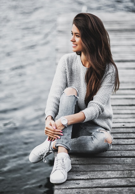 Belle femme rêveuse assise sur la jetée au bord du lac.