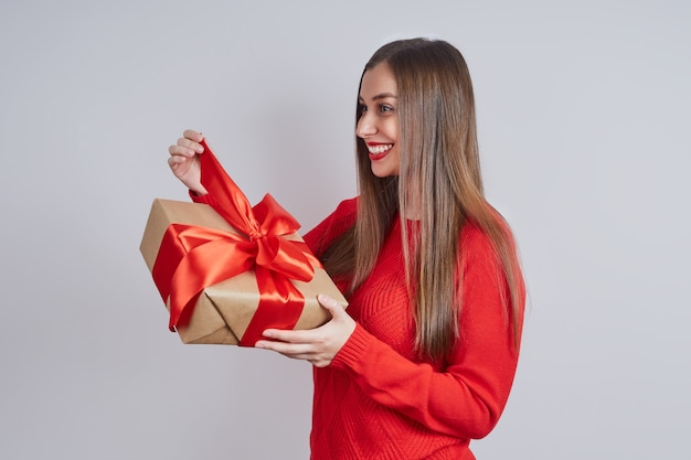 Belle femme en riant dans un pull rouge, délie un arc sur une boîte cadeau