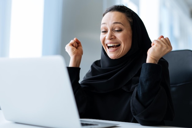 Belle femme avec une robe abaya travaillant sur son ordinateur. Employée d'âge moyen au travail dans un bureau d'affaires à Dubaï. Concept sur les cultures et le mode de vie du Moyen-Orient