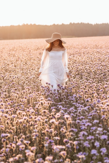 Belle femme en robe blanche dans un champ de lavande au coucher du soleil