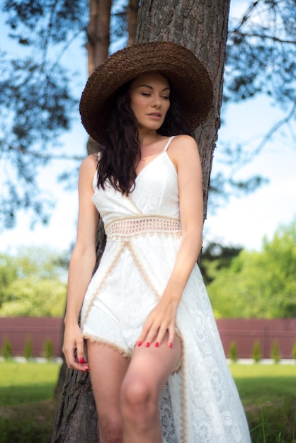 Belle femme en robe d'été blanche et chapeau de paille dans le jardin