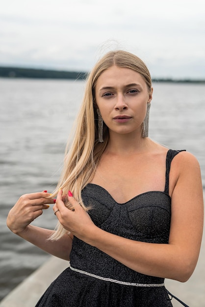 Belle femme en robe de mode noire posant près de l'heure d'été du lac