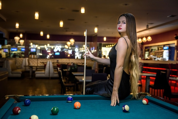 Belle femme en robe noire posant avec queue de billard