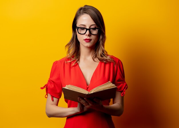 Belle femme en robe rouge avec un livre sur le mur jaune