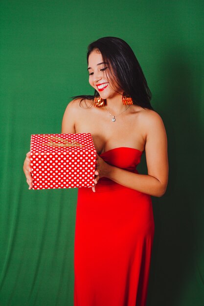 Belle femme en robe rouge tenant un cadeau. Studio tourné avec fond vert... Noël.