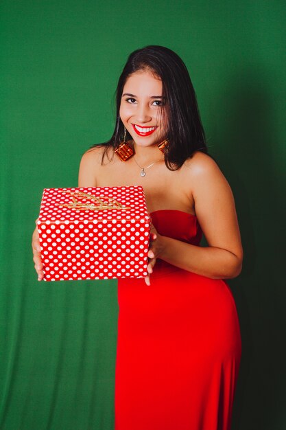 Belle femme en robe rouge tenant un cadeau. Studio tourné avec fond vert... Noël.