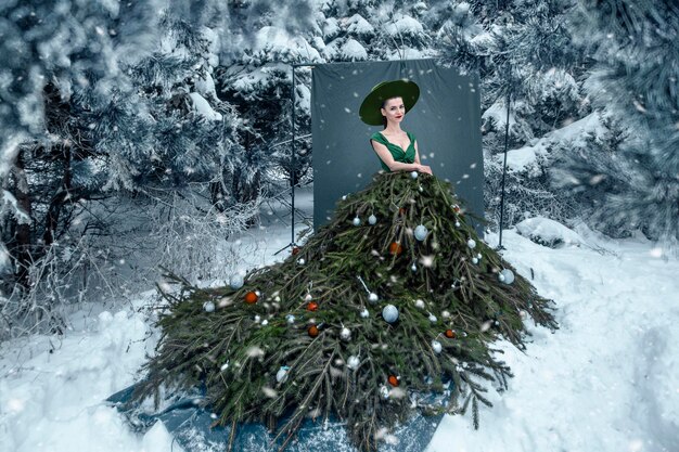 Belle femme avec une robe de sapin de noël dans la forêt d'hiver