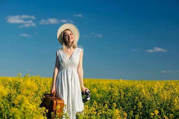 Belle femme en robe avec valise dans le champ de colza