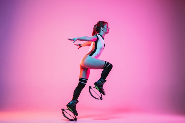 Belle femme rousse dans un vêtement de sport rouge sautant dans un kangoo saute des chaussures