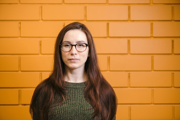 Belle femme rousse à lunettes sur mur de briques jaunes