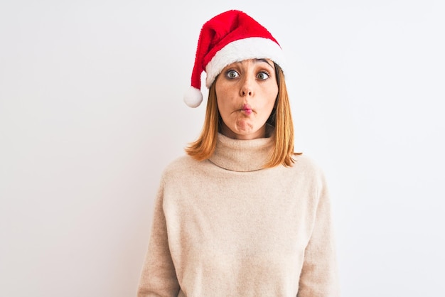 Belle femme rousse portant un chapeau de Noël sur fond isolé faisant face au poisson avec des lèvres geste fou et comique Expression drôle