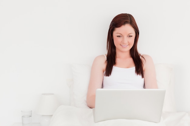 Belle femme rousse se détendre avec son ordinateur portable tout en étant assis sur son lit